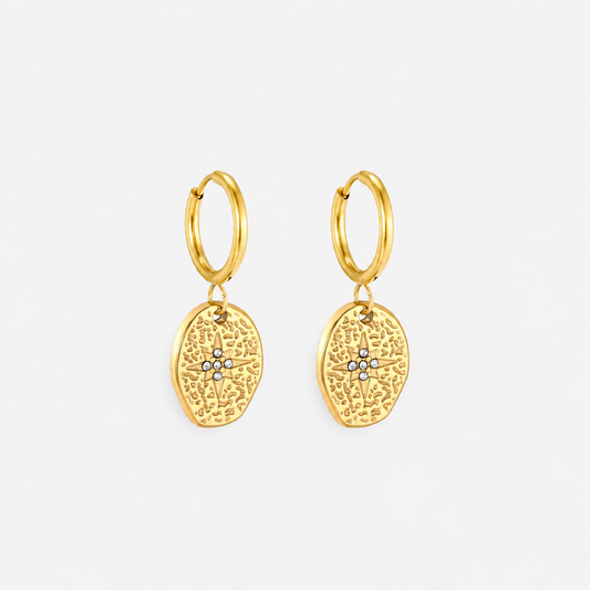A pair of gold huggie hoop earrings with textured, organic-shaped dangles featuring a small central cluster of clear stones, shown on a light gray background.