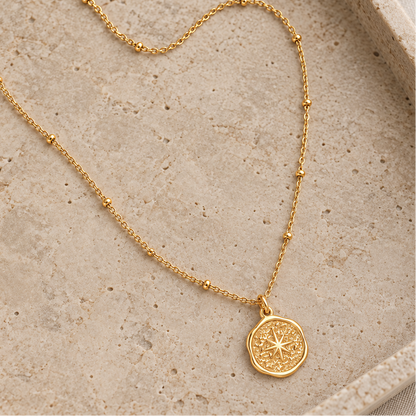 Sol Necklace gold satellite chain and starburst pendant on a natural stone tray