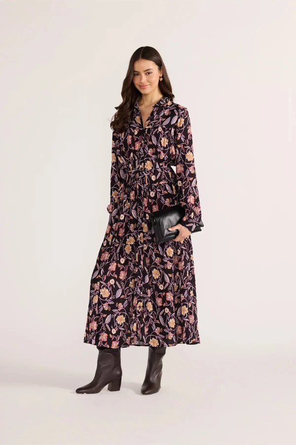 Woman wearing a floral dress holding a clutch against a white background