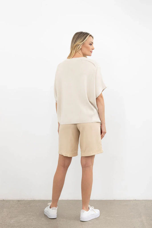 Woman wearing a beige outfit with shorts and a top against a white background