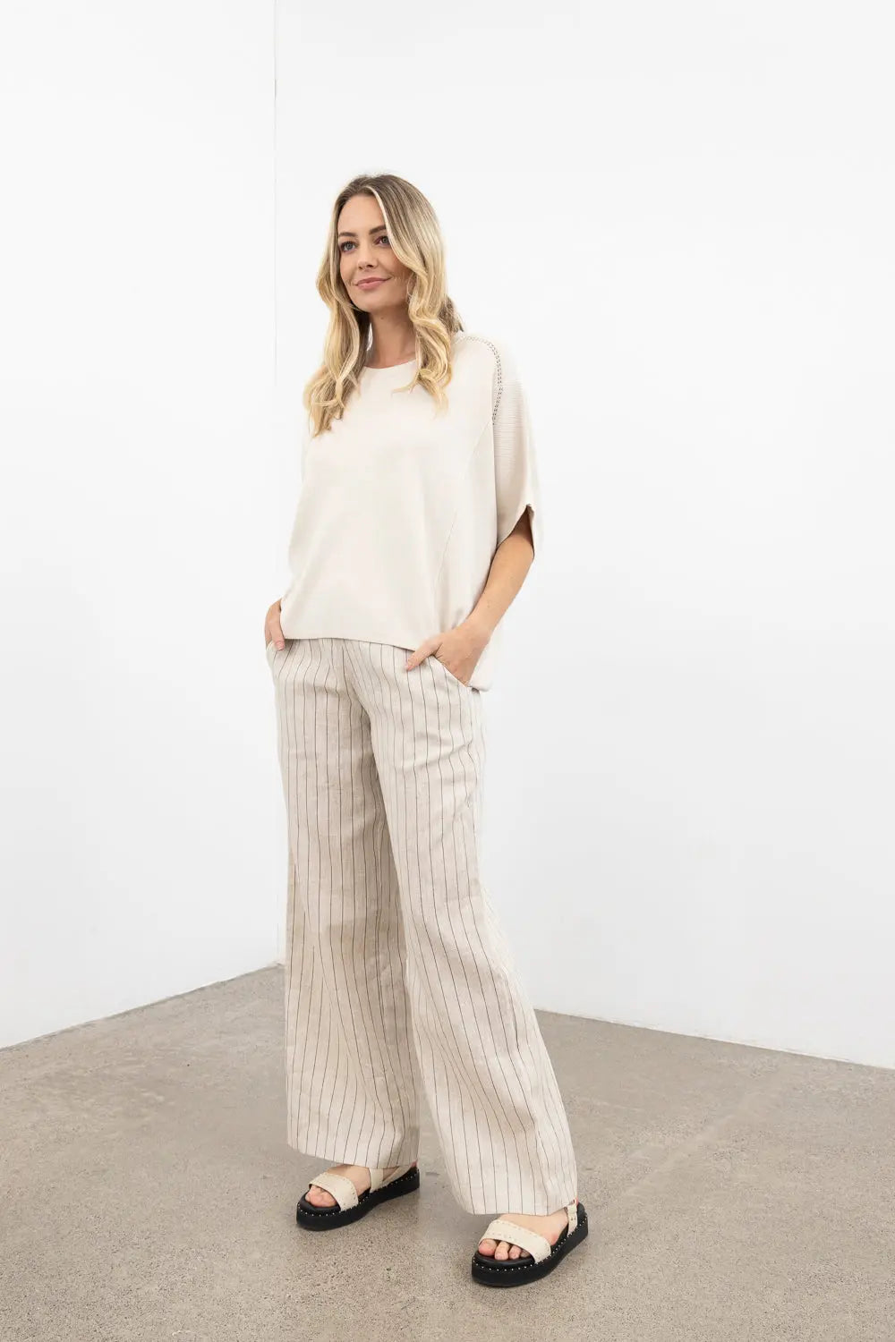Woman wearing a beige top and striped pants against a white background