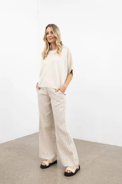 Woman wearing a beige top and striped pants against a white background