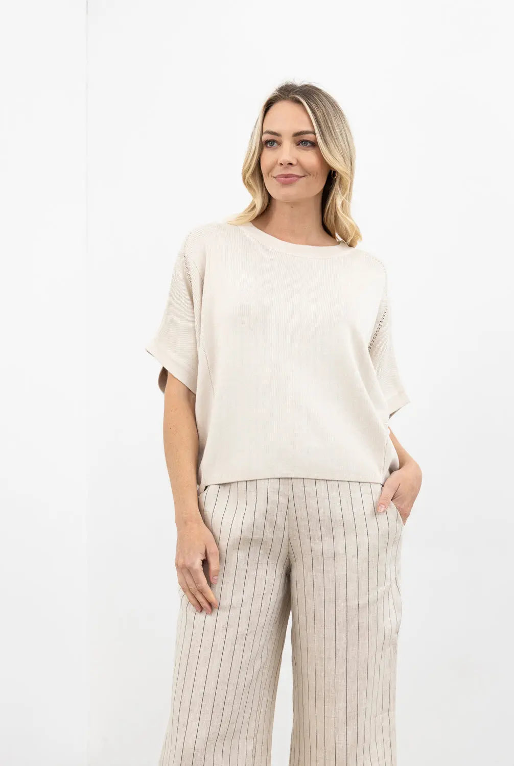 Woman wearing a beige top and striped pants on a white background
