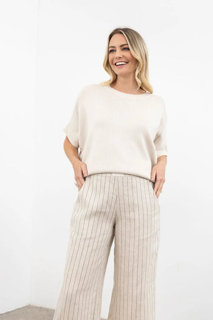 Woman wearing a white sweater and beige striped pants against a white background