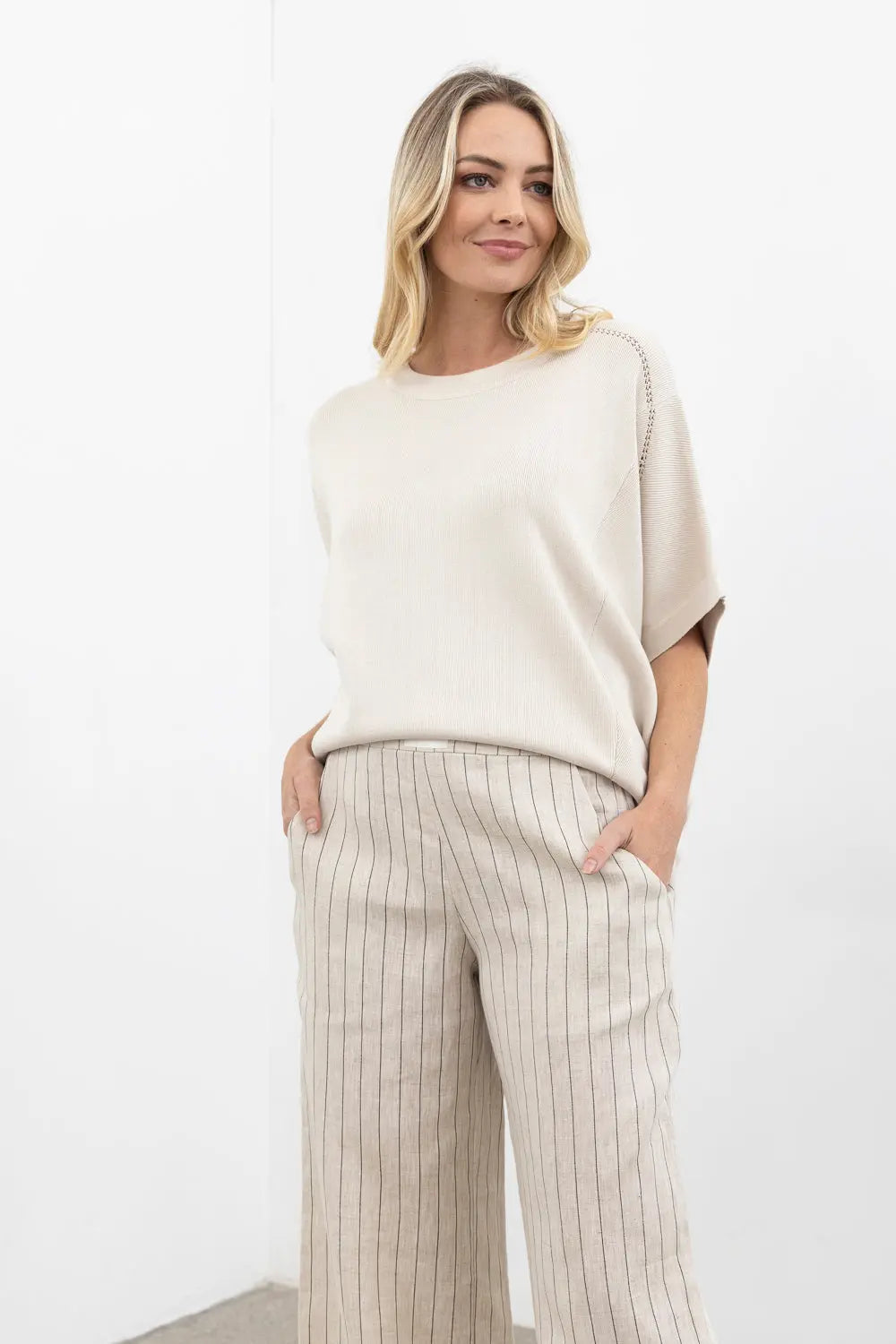 Woman wearing a cream-colored top and striped pants on a white background