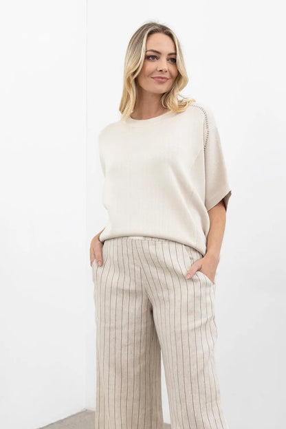Woman wearing a cream-colored top and striped pants on a white background