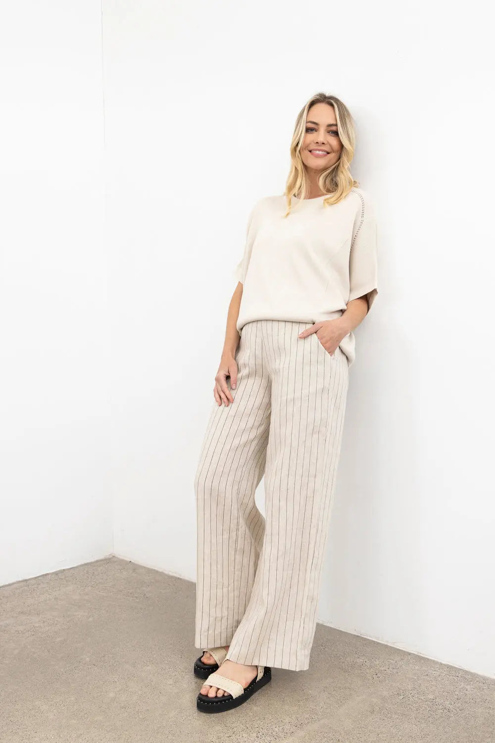 Woman wearing a white top and striped pants against a white wall.