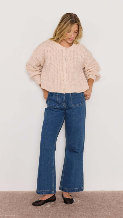Woman wearing a light pink sweater and blue jeans against a white background