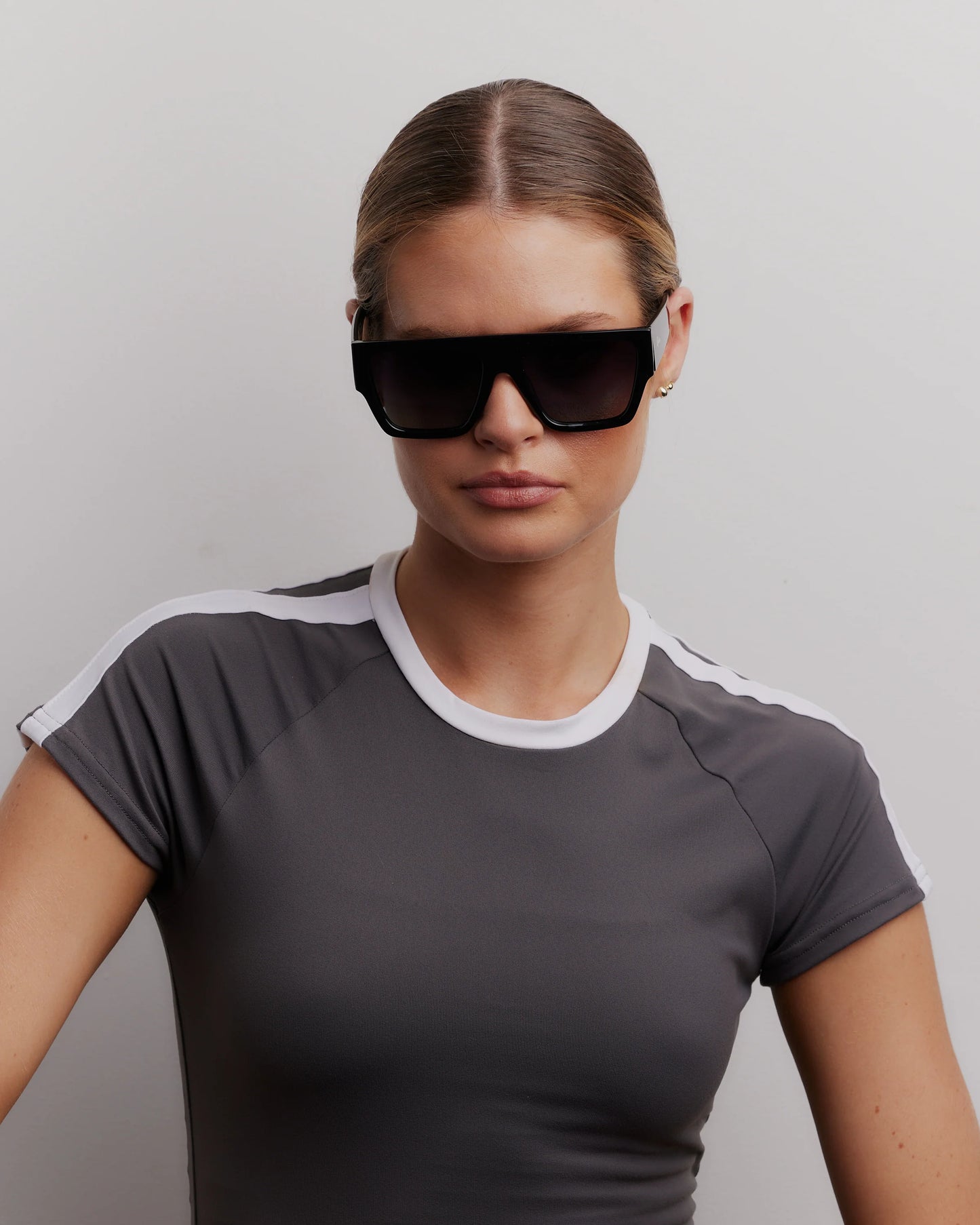 Woman wearing a gray t-shirt with white trim and black sunglasses against a plain background
