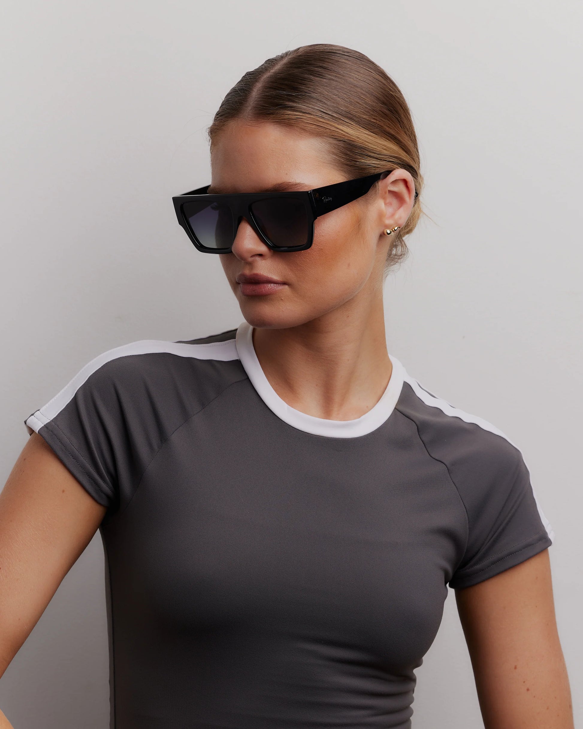 Woman wearing a gray athletic shirt with white accents and black sunglasses against a plain background
