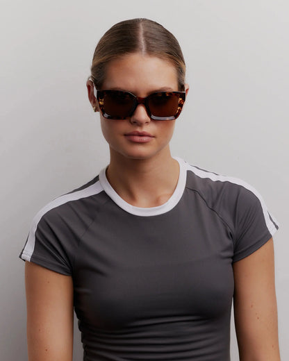 Woman wearing a gray and white sports outfit with sunglasses on a plain background
