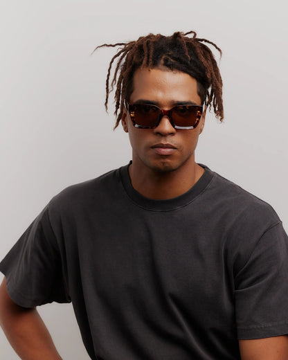 Man wearing sunglasses and a black t-shirt against a plain background
