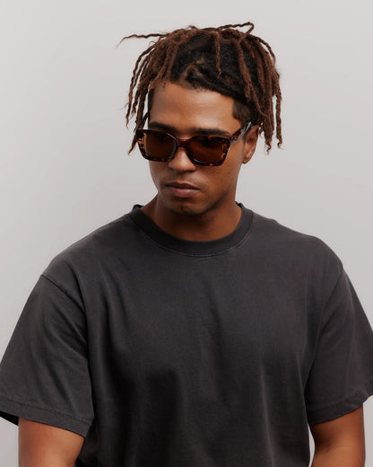 Man wearing sunglasses and a black t-shirt against a gray background