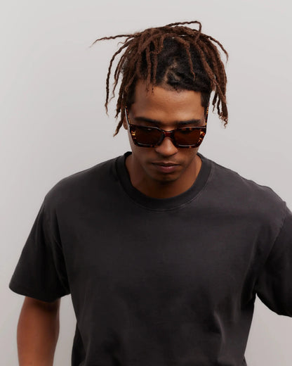 Man wearing sunglasses and a black t-shirt against a plain background