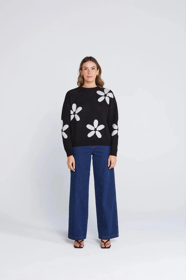 Model wearing the Petal Jumper by Thing Thing — black cotton knit sweater with oversized white petal motifs, styled with wide-leg blue trousers.