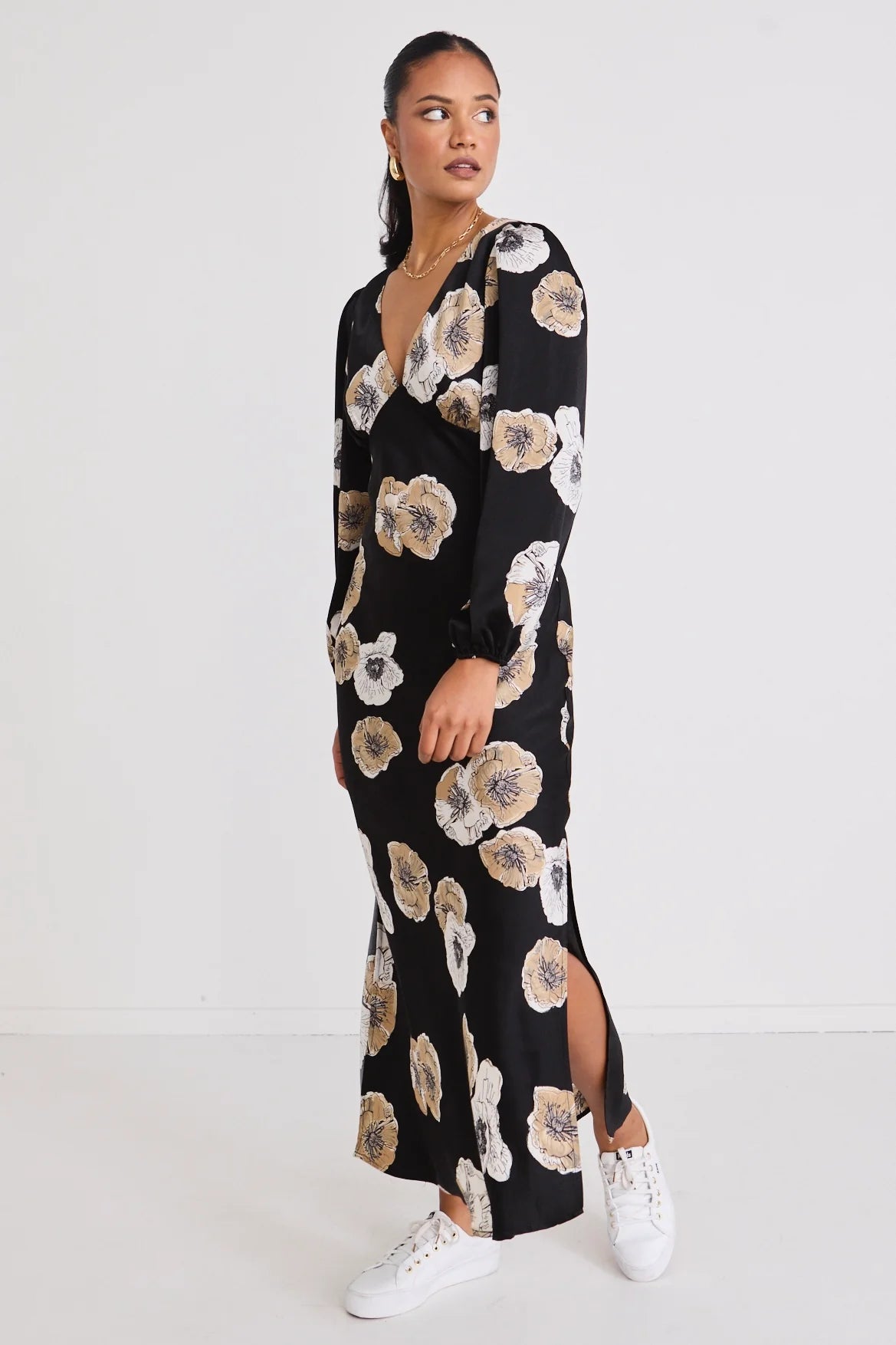 Woman wearing a black floral dress with white sneakers on a white background