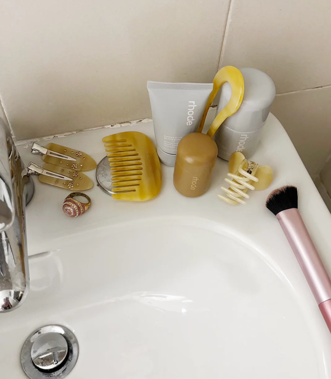 Assorted hair care products on a bathroom sink. Buttermilk Maddie Creaseless Clips Shortbread Honey Dark Roast - The Rose Edit
