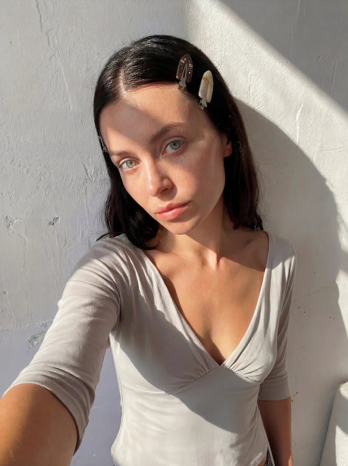 Woman wearing a beige top against a white wall. Buttermilk Maddie Creaseless Clips Shortbread Honey Dark Roast - The Rose Edit