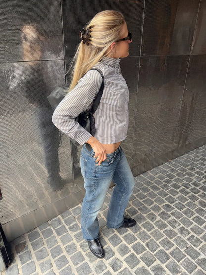 Woman standing against a reflective wall wearing a striped shirt and jeans. Buttermilk Rebekah Claw Clip Coffee Table - The Rose Edit