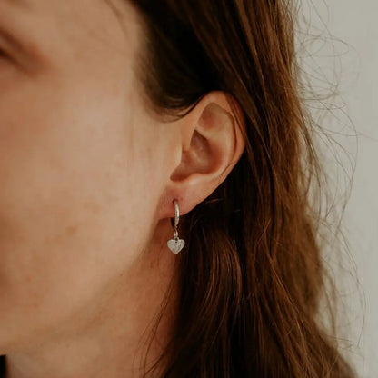 Silver heart hoop earring worn on model — close-up ear shot. heart hoop earrings KatyB Jewellery