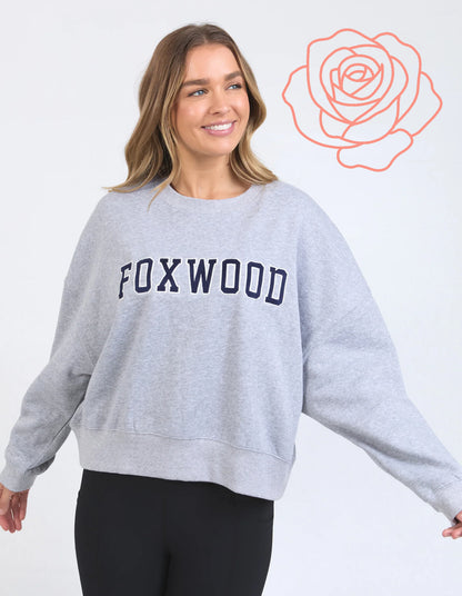 Woman wearing a gray sweatshirt with 'FOXWOOD' text, standing against a white background with a rose graphic.