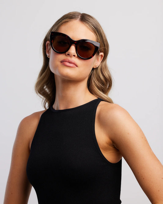 Woman wearing sunglasses and a black sleeveless top against a light gray background