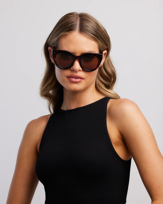 Woman wearing black sunglasses and a black sleeveless top against a light gray background