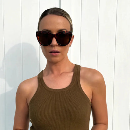 Woman wearing sunglasses and a brown tank top against a white background