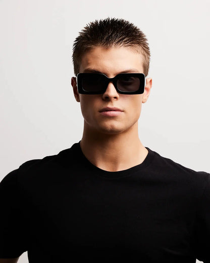 Man wearing black sunglasses and a black t-shirt against a light gray background