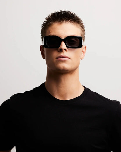 Man wearing black sunglasses and a black t-shirt against a light gray background