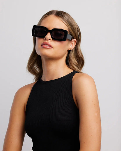 Woman wearing black sunglasses and a black top against a light gray background