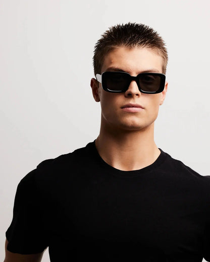 Person wearing black sunglasses and a black shirt against a light gray background