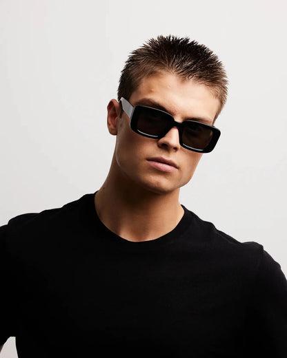 Person wearing black sunglasses and a black shirt against a light gray background