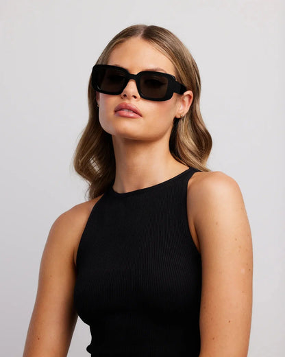 Woman wearing black sunglasses and a black top against a light gray background