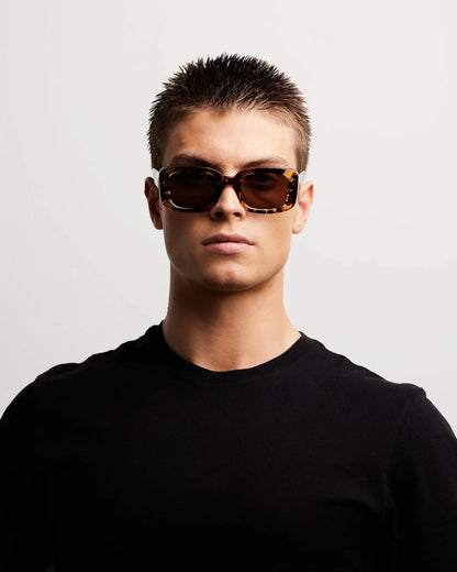 Person wearing sunglasses and a black shirt on a light gray background