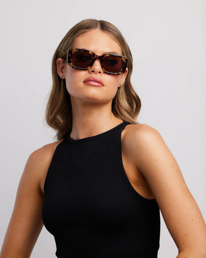 Woman wearing brown sunglasses and a black sleeveless top against a light gray background