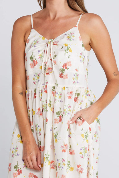 Woman wearing a floral dress with a plain background. Zinnia Dress Summer Haven Detail View - The Rose Edit
