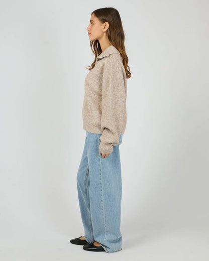 Person wearing a beige sweater and light blue jeans on a white background. Bonni Knit Quarter Zip Jumper Brown - The Rose Edit