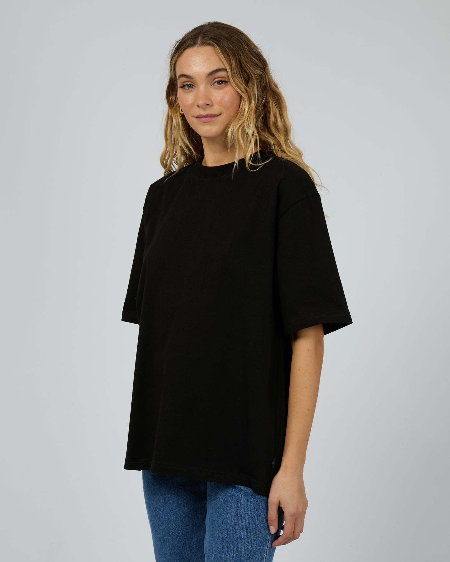 Woman wearing a black oversized t-shirt and blue jeans on a plain background