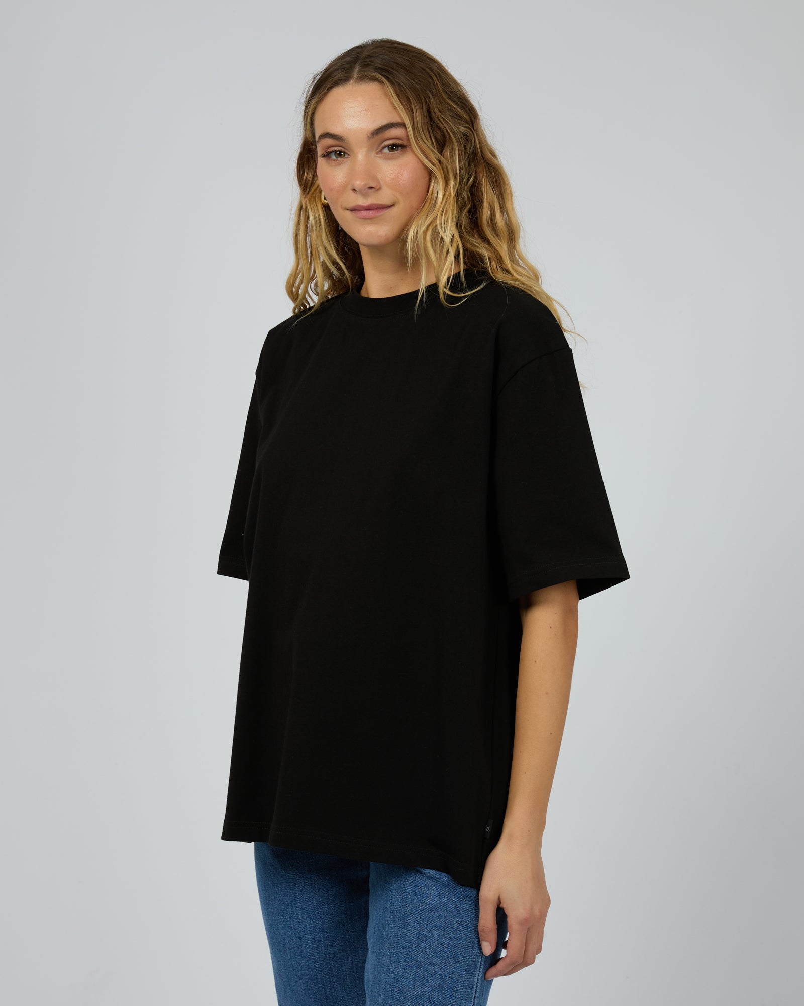 Woman wearing a black oversized t-shirt and blue jeans on a plain background