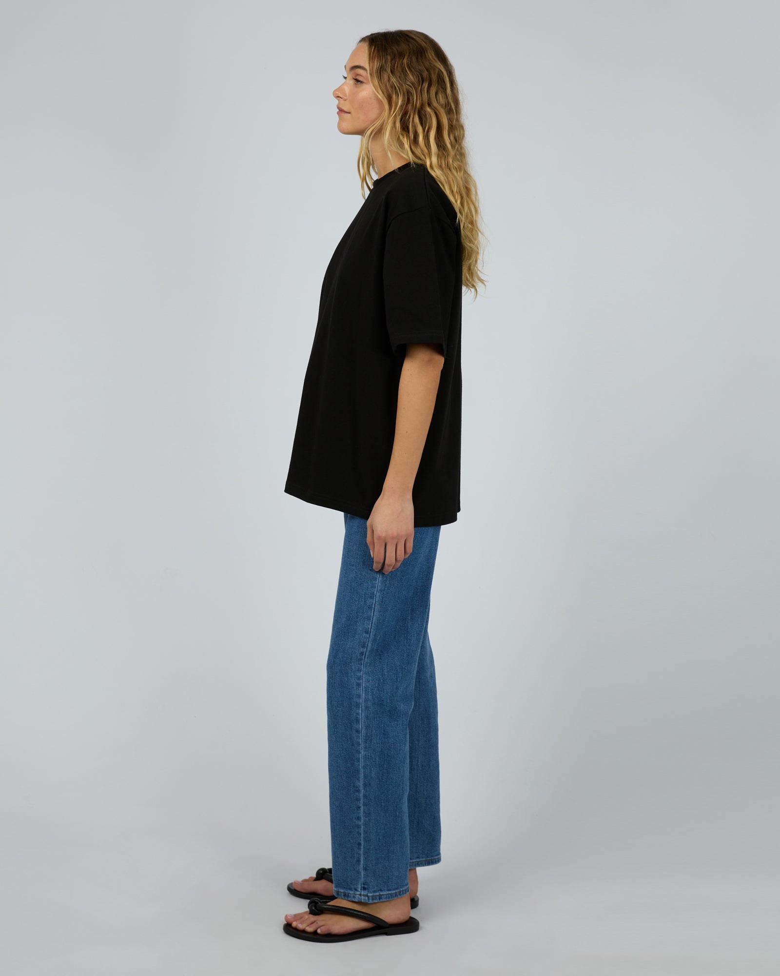 Person wearing a black t-shirt and blue jeans standing against a plain background