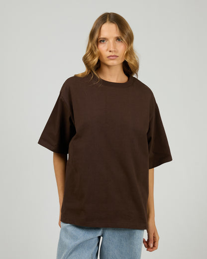 Person wearing a brown oversized t-shirt on a plain background. Core Oversized Tee Chocolate - The Rose Edit