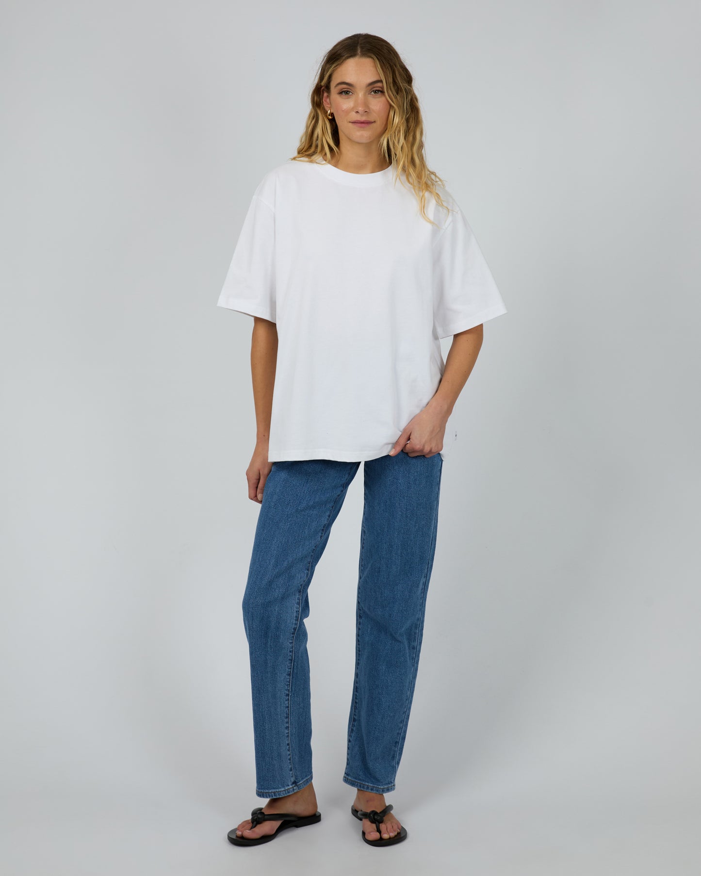 Woman wearing a white oversized t-shirt and blue jeans on a plain background