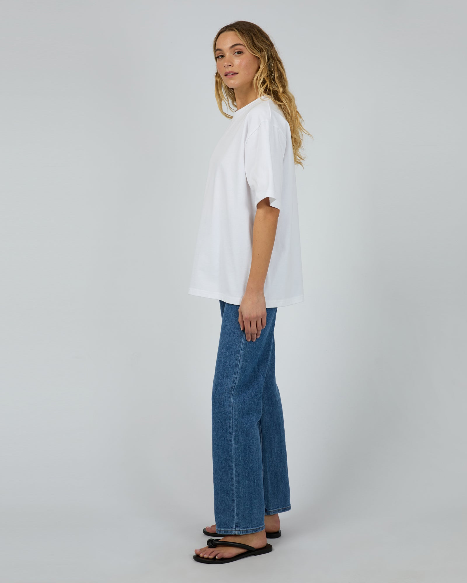 Woman wearing a white shirt and blue jeans on a plain background
