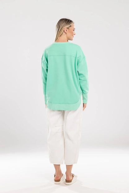 Person wearing a light green sweater and white pants on a white background.Ena Sweat Green - The Rose Edit