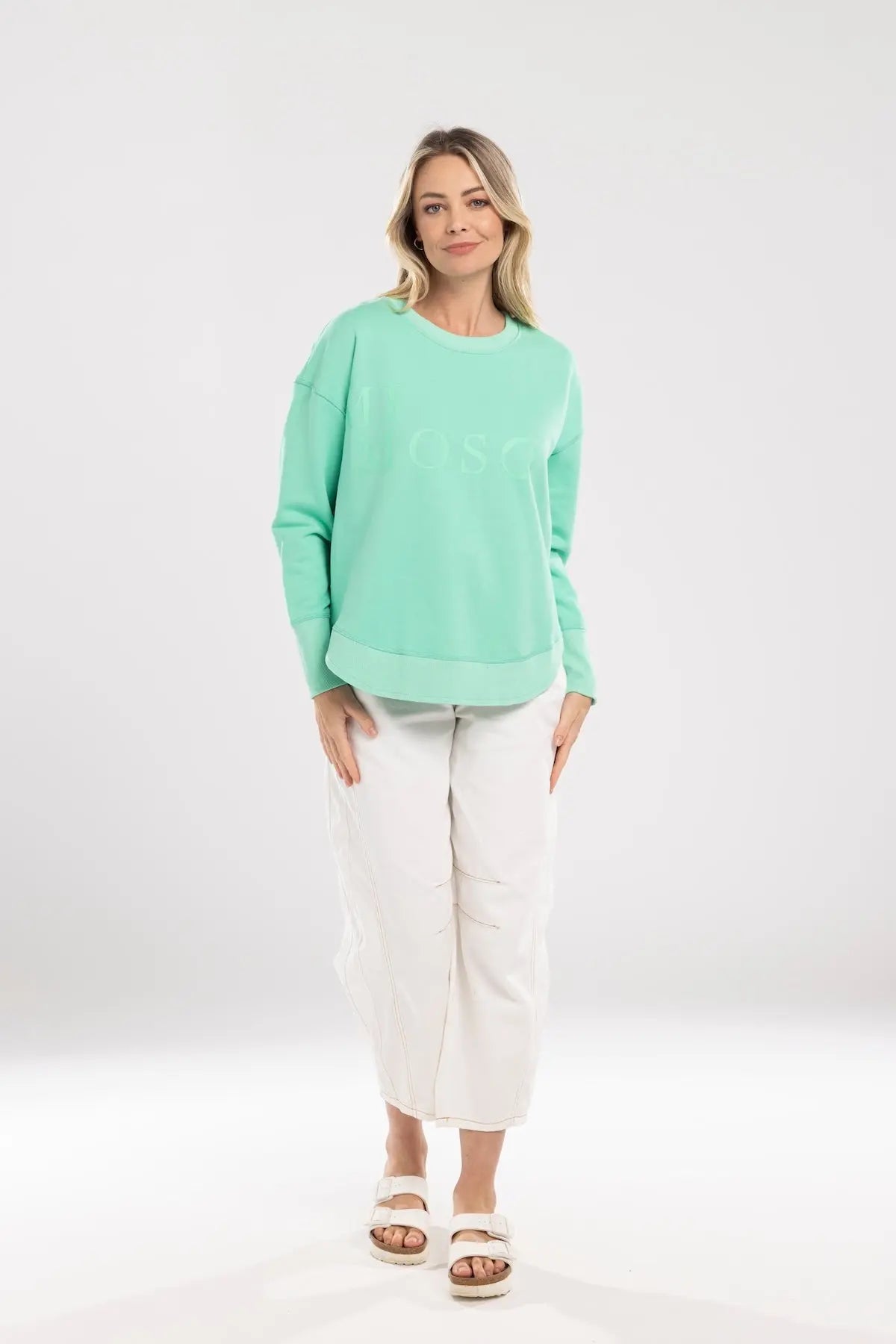 Woman wearing a light green sweater and white pants on a white background