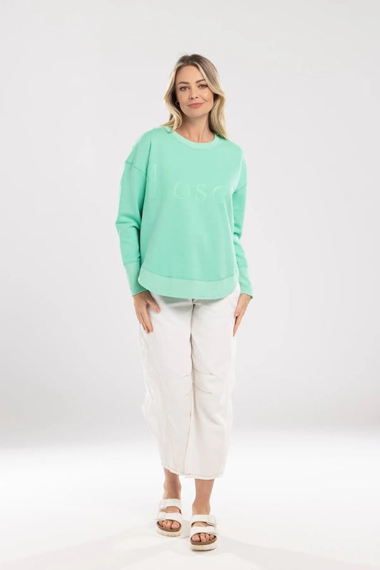 Woman wearing a light green sweater and white pants on a white background