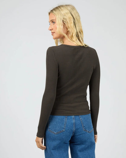 Person wearing a black long-sleeve top and blue jeans on a plain background. All About Eve Eve Rib Baby Long Sleeve Tee Washed Black - The Rose Edit