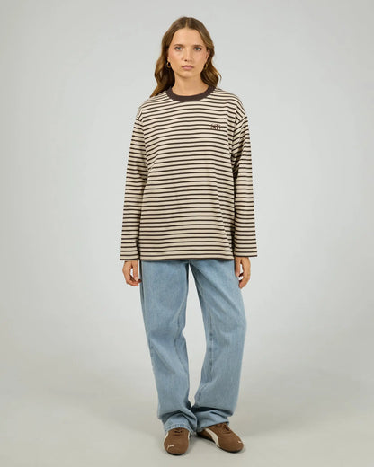 Person wearing a striped long-sleeve shirt and blue jeans on a plain background.Silent Theory Foundation Stripe Long Sleeve Tee Chocolate - The Rose Edit