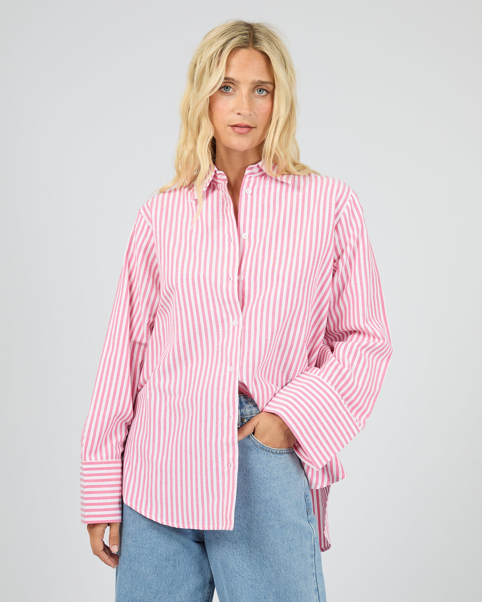 Woman wearing a pink and white striped shirt with blue jeans on a gray background